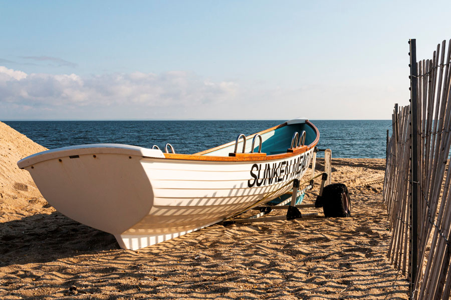  White lifeguards row boat on the sand next to a fence at Sunken Meadow State Park with the Long Island Sound in the background.